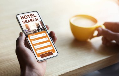 Siyah adam elinde akıllı telefonuyla otel arama başvurusu yapıyor, kahve içiyor.