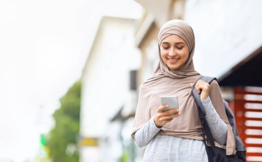 Sırt çantalı, akıllı telefon kullanan pozitif müslüman kız