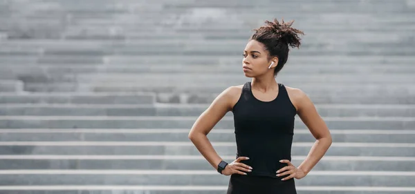 Ejercicios de footing y estilo de vida saludable. Seriamente afroamericana chica en ropa deportiva con rastreador de fitness en el fondo de escaleras grises —  Fotos de Stock