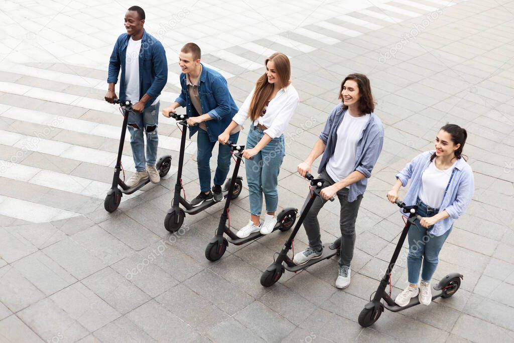 Five friends having ride on electric kick scooters