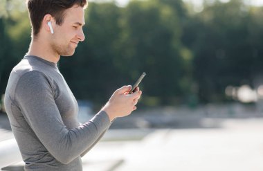 Sabah antrenmanına müzikle başla. Kulaklıklı gülümseyen adam akıllı telefona bakar.