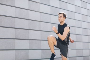 Şehir tarzı. Fitness takip cihazı olan bir adam spor için gri duvar arkasına gider.