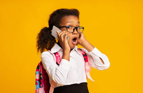Sorprendido colegiala africana hablando en el teléfono celular de pie sobre fondo amarillo — Foto de Stock