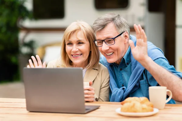 Радостный пожилой человек и его жена общаются с семьей или друзьями на ноутбуке в кемпинге — стоковое фото