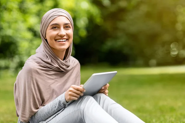 Mujer musulmana feliz usando tableta digital, descansando al aire libre — Foto de Stock