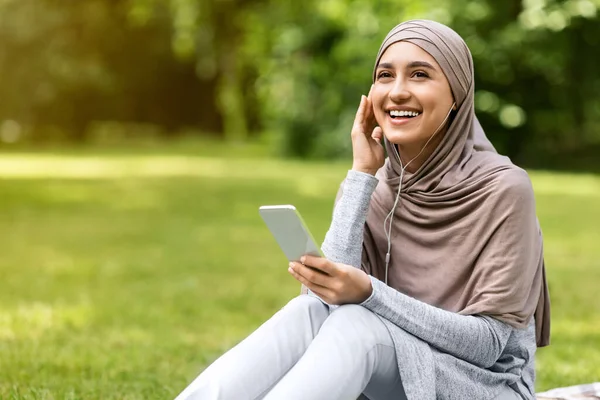 Gadis muslim yang suka bercanda mendengarkan musik, menggunakan earphone dan smartphone — Stok Foto