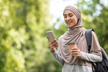 Genç Arap kadın kahve içiyor ve telefon kullanıyor.