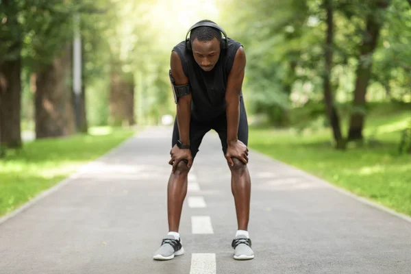 Müder afrikanischer Sportler ruht sich vor verschwommenem Park-Hintergrund aus — Stockfoto