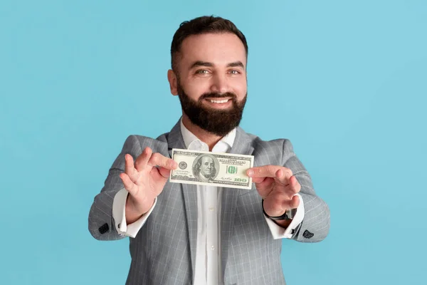 Feliz empresario milenario mostrando billete de cien dólares sobre fondo azul — Foto de Stock