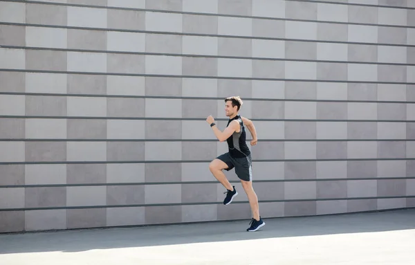 Training en hardlopen in de stad in de ochtend. Millennial man in sportkleding en fitness tracker loopt en springt — Stockfoto
