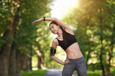 Sportif Asyalı kız parkta koşmadan önce egzersiz yapıyor, dışarıda kaslarını esnetiyor.