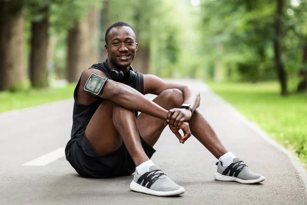 Feliz chico deportivo descansando después de trotar, sentado en el camino —  Fotos de Stock