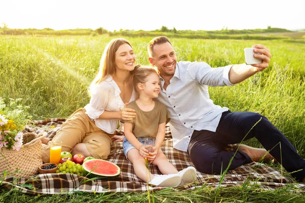 Família feliz tomando selfie sentado no campo — Fotografia de Stock