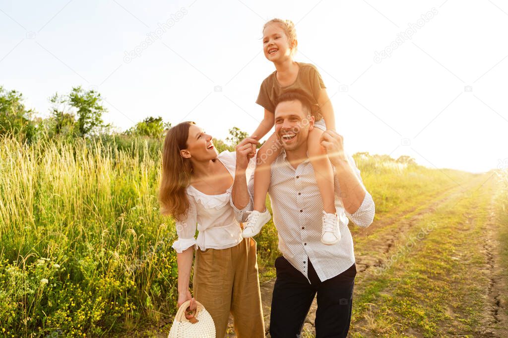 Happy parents and kid walking together outdoor in summer forest, father riding his daughter on neck, copy space