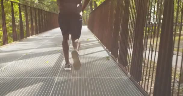 Chico afroamericano corriendo en el puente en el parque de la ciudad, vista trasera — Vídeo de stock
