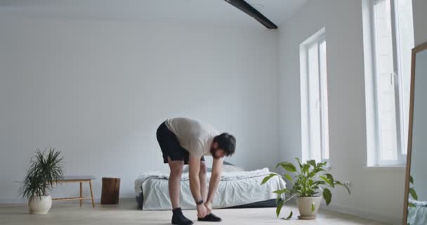 Тысячелетний парень делает упражнения на растяжку дома — стоковое видео