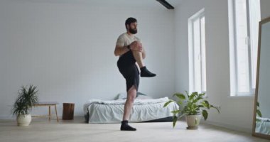 Genç sakallı adam bacak egzersizi yapıyor.