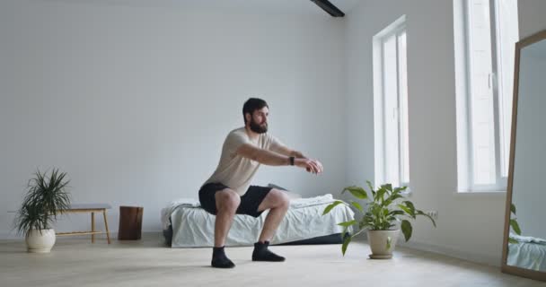 Junger bärtiger Mann macht Kniebeugen-Übungen zu Hause — Stockvideo