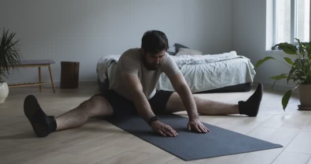 Hombre joven estirando las piernas, ejercitándose en el suelo en casa — Vídeos de Stock