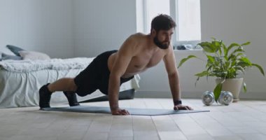 Evde yerde şınav çeken genç sakallı adam.