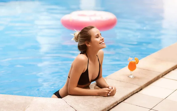 Retrato de bela mulher bronzeada em roupa de banho preta relaxando na piscina no dia quente de verão — Fotografia de Stock