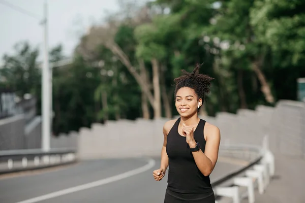 Girl runs in summer at city. Woman with fitness tracker runs along track — Stock Photo, Image