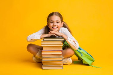 Küçük Liseli Kız Sırıtan Kitap Yığını 'nda oturuyor, Sarı Arka plan