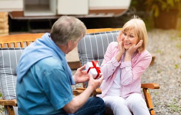 Senior man giving present to his lovely wife near camper van outside — Stock Photo, Image