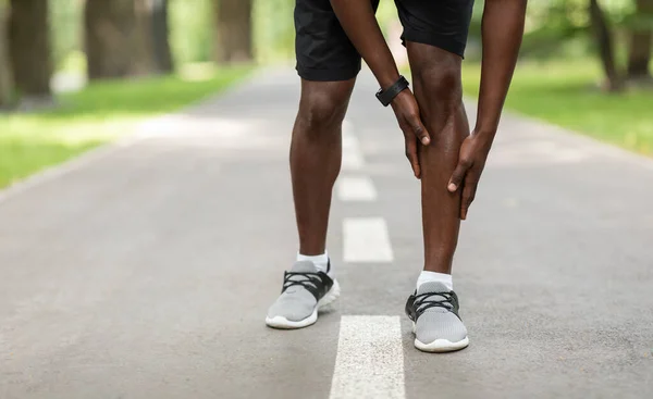 Schwarzer Sportler berührt beim Joggen im Freien sein schmerzendes Bein — Stockfoto