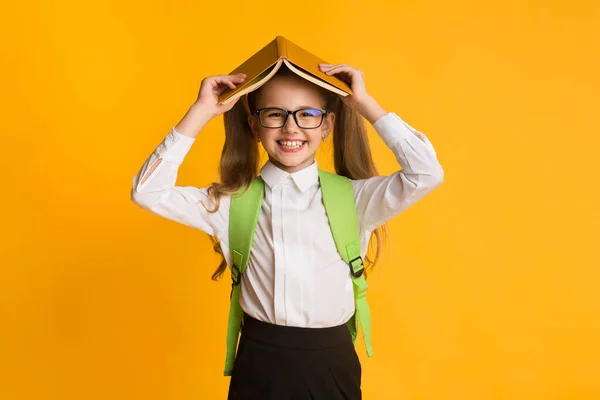 Ragazza allegra della scuola che copre la testa con la posa del libro, sfondo giallo — Foto Stock