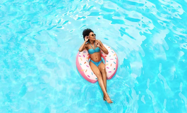 若いアフリカ系アメリカ人女性リラックスオンドーナツインフレータブルリングでホテルリゾートプール,オーバーヘッドビュー — ストック写真