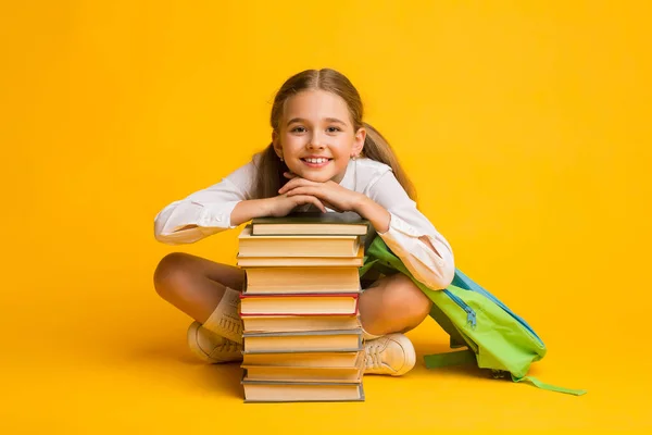 Pequena aluna sorrindo sentada na pilha de livros, fundo amarelo — Fotografia de Stock