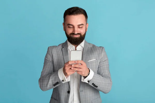 Handsome bearded entrepreneur searching web for business data on blue background — Stock Photo, Image