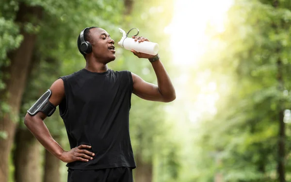 Durstiger schwarzer Sportler trinkt Wasser, joggt im Park — Stockfoto