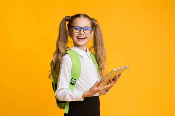 Gelukkig schoolmeisje Holding digitale tablet poseren over gele studio achtergrond — Stockfoto