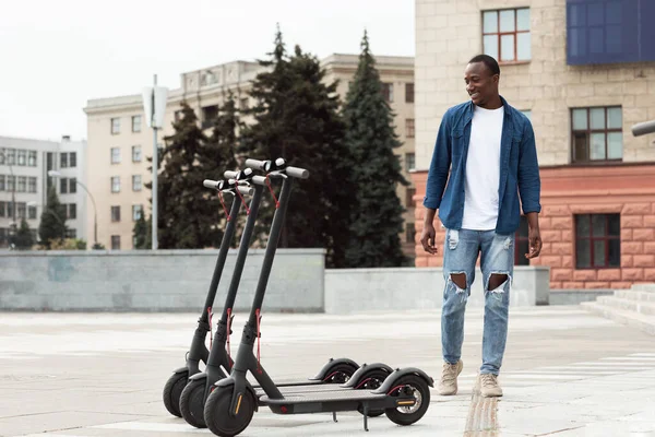 Kerel staande en kijkend naar verhuur gemotoriseerde kick scooters — Stockfoto