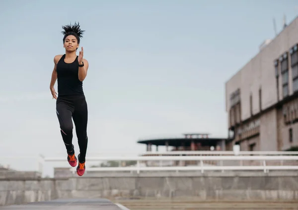 Correr, saltar e voar. Atlético slim afro-americano menina na moda esporte uniforme congelado no ar — Fotografia de Stock