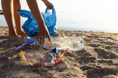 Gönüllü, kirletilmiş plajda atık plastik topluyor.