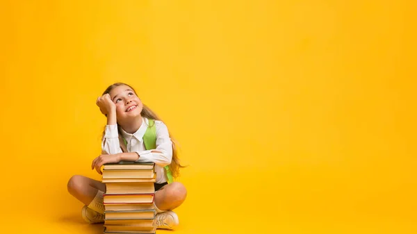 Schoolmeisje dromen zitten aan boeken stapelen over gele achtergrond, Panorama — Stockfoto