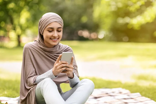 Hermosa chica árabe usando un teléfono inteligente moderno, pasar tiempo en el parque —  Fotos de Stock