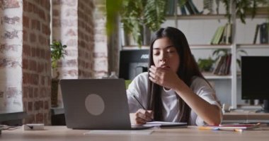 Asyalı öğrenci kız esniyor, dizüstü bilgisayarda Webinar izlerken uyuyakalıyor.