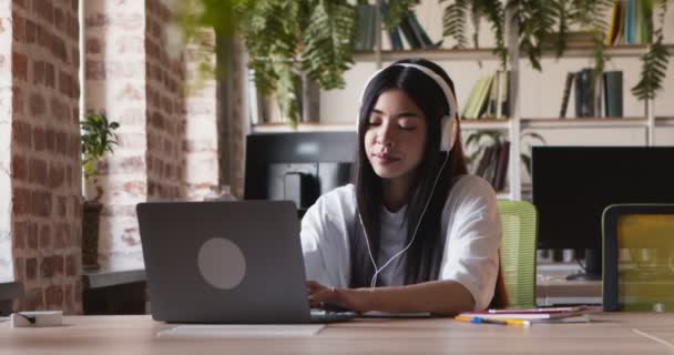 戴耳机在笔记本电脑上听音乐的亚洲女学生 — 图库视频影像