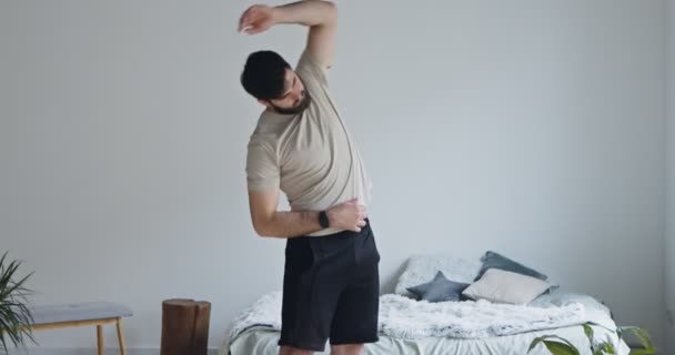 Mladý vousatý chlap trénuje doma, cvičí na protahování — Stock video