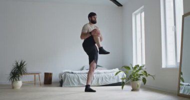 Genç sakallı adam bacak egzersizi yapıyor.