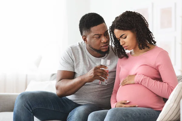 Negro esperando mujer sintiéndose enfermo, marido dando vaso de agua — Foto de Stock