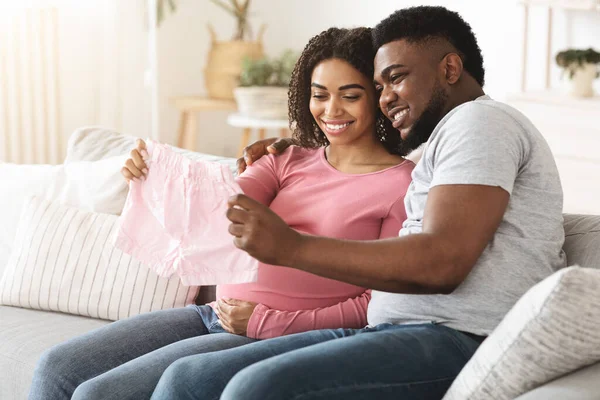 Sonriente negro esperando pareja sosteniendo bebé ropa — Foto de Stock