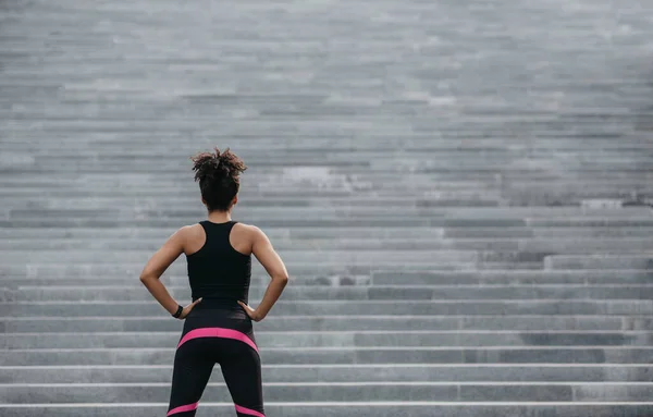 Comienza a entrenar. Chica en ropa deportiva se ve en la gran escalera de la ciudad gris —  Fotos de Stock