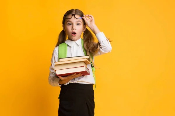 Překvapená školačka při pohledu na kameru drží zásobník knih, Studio — Stock fotografie