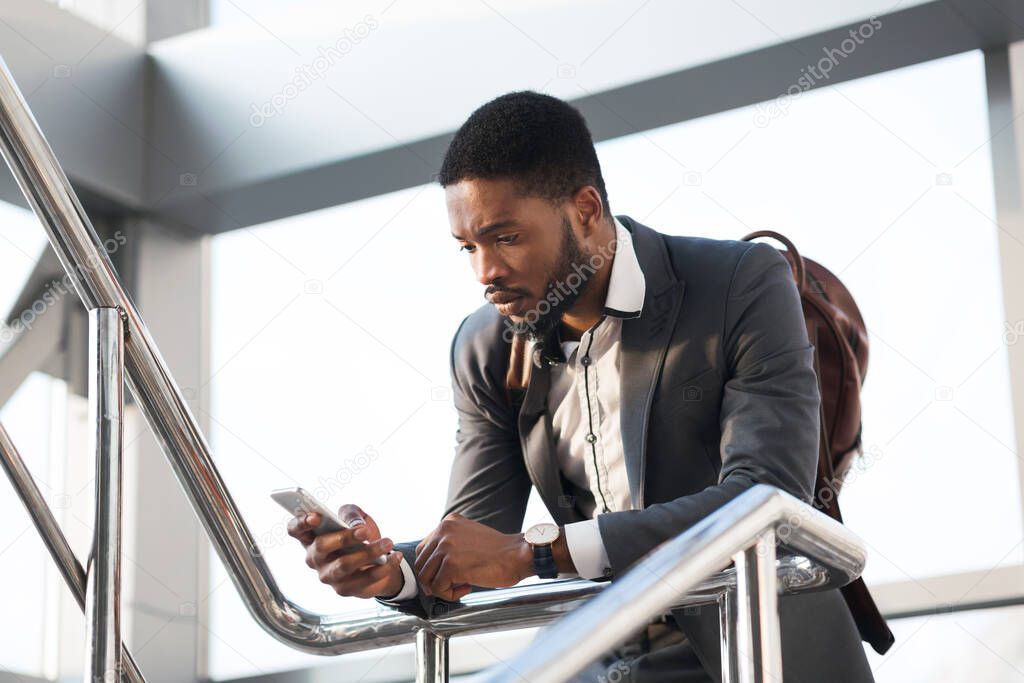 Black Business Guy Using Cellphone Standing At Rail Station