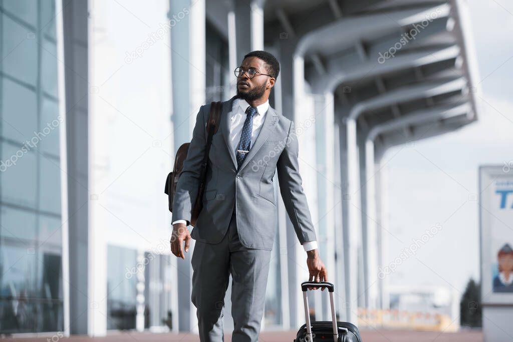 Black Businessman Traveler Walking With Suitcase Near Rail Station Outdoors